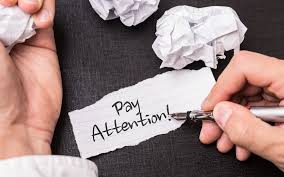 person writing "pay attention" on paper to refer to writing headlines
